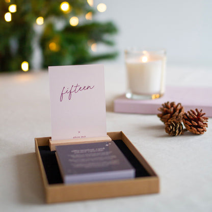 affirmation card advent calendar, showing card number 15 standing in the wooden display stand, christmas tree lights sparkle in the background